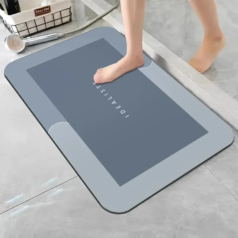 A gray diatomaceous earth absorbent bath mat is placed on a light gray floor next to a person's bare foot.