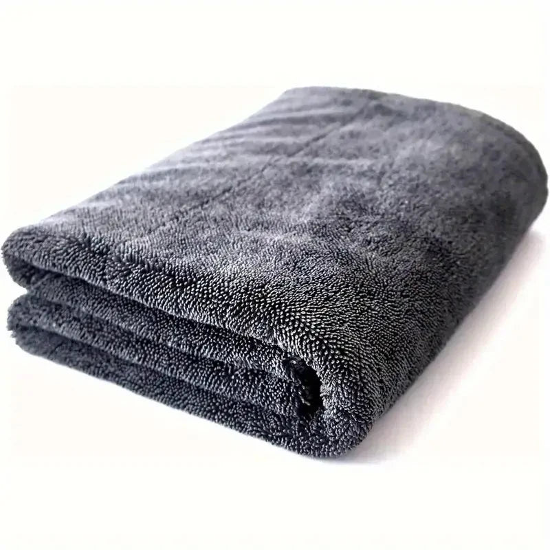 A dark gray microfiber car cleaning towel rolled up on a white surface.