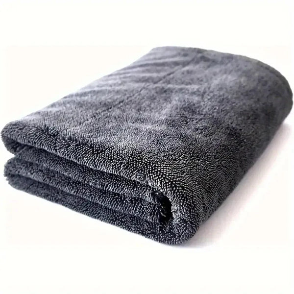A dark gray microfiber car cleaning towel rolled up on a white surface.