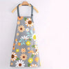 Gray apron with a floral print featuring yellow, orange, and white daisies on a wooden hanger.