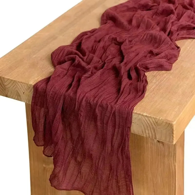 A deep maroon boho cheesecloth table runner draped over a light wooden table.
