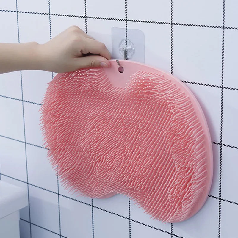 Eine Hand hängt eine rosa Silikon-Saug-Füßnagelmassagematte an eine weiße Fliesenwand.