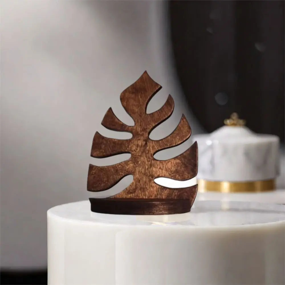 A dark brown wooden leaf wall art frame displayed on a white pedestal.