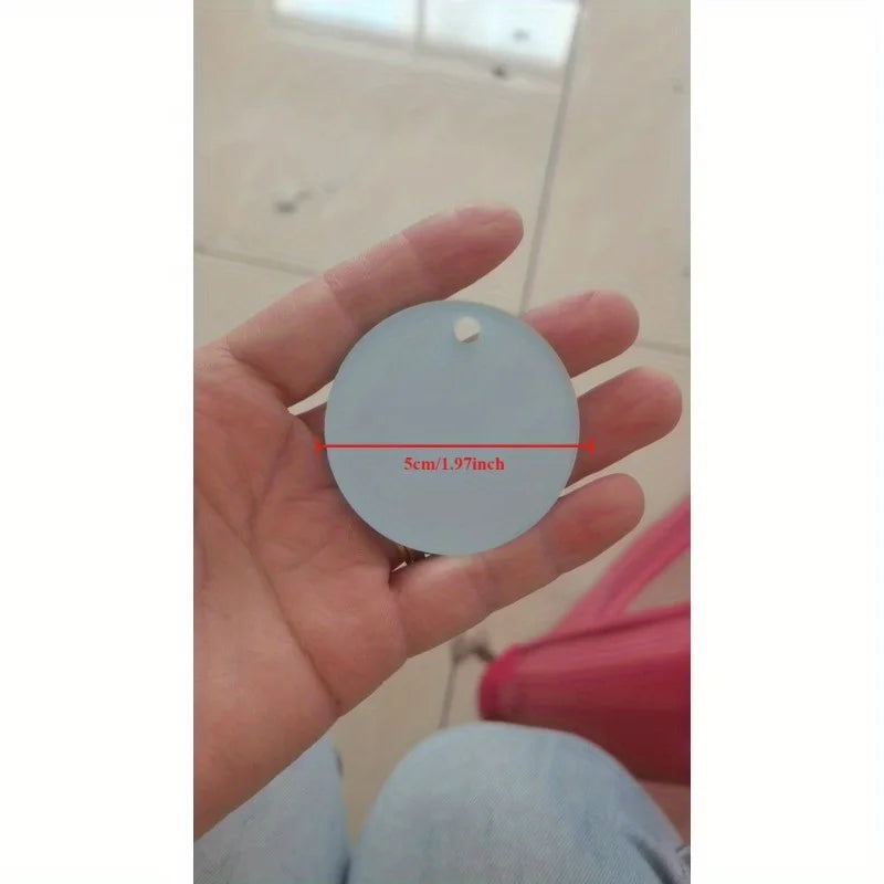 A hand holds a round, gray acrylic keychain with a hole for a photo or logo inside.