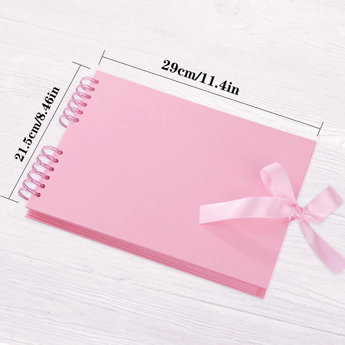 Álbum de scrapbooking rosa personalizable con encuadernación espiral mostrado sobre una superficie de madera blanca.
