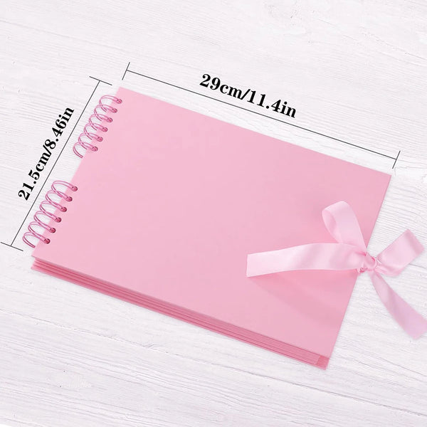 A pink customizable scrapbook album with spiral binding is shown on a white wooden surface.
