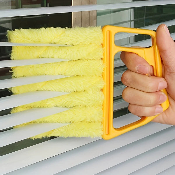 A hand holds a yellow cleaning brush with white bristles, used for cleaning window blinds.