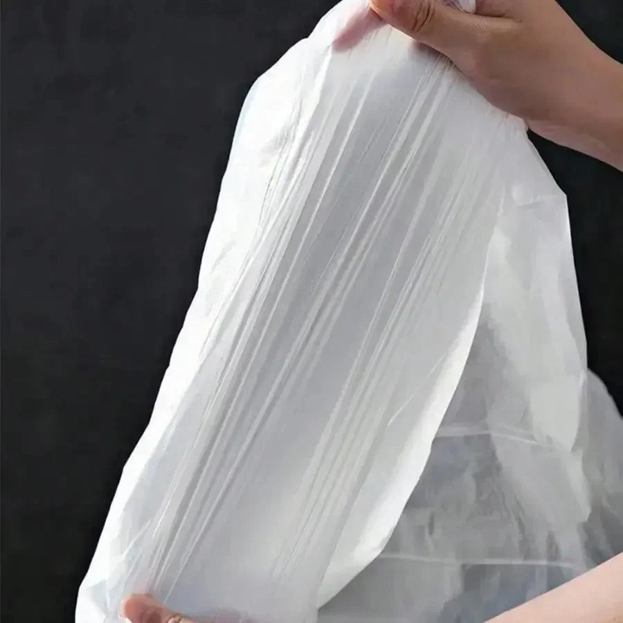 A hand is holding a clear plastic drawstring trash bag, showing its translucent material.