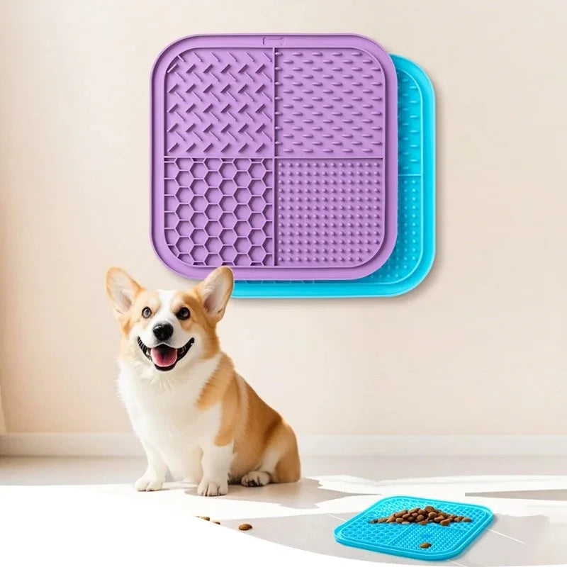 A happy dog sits next to purple and blue silicone lick mats on a white floor.