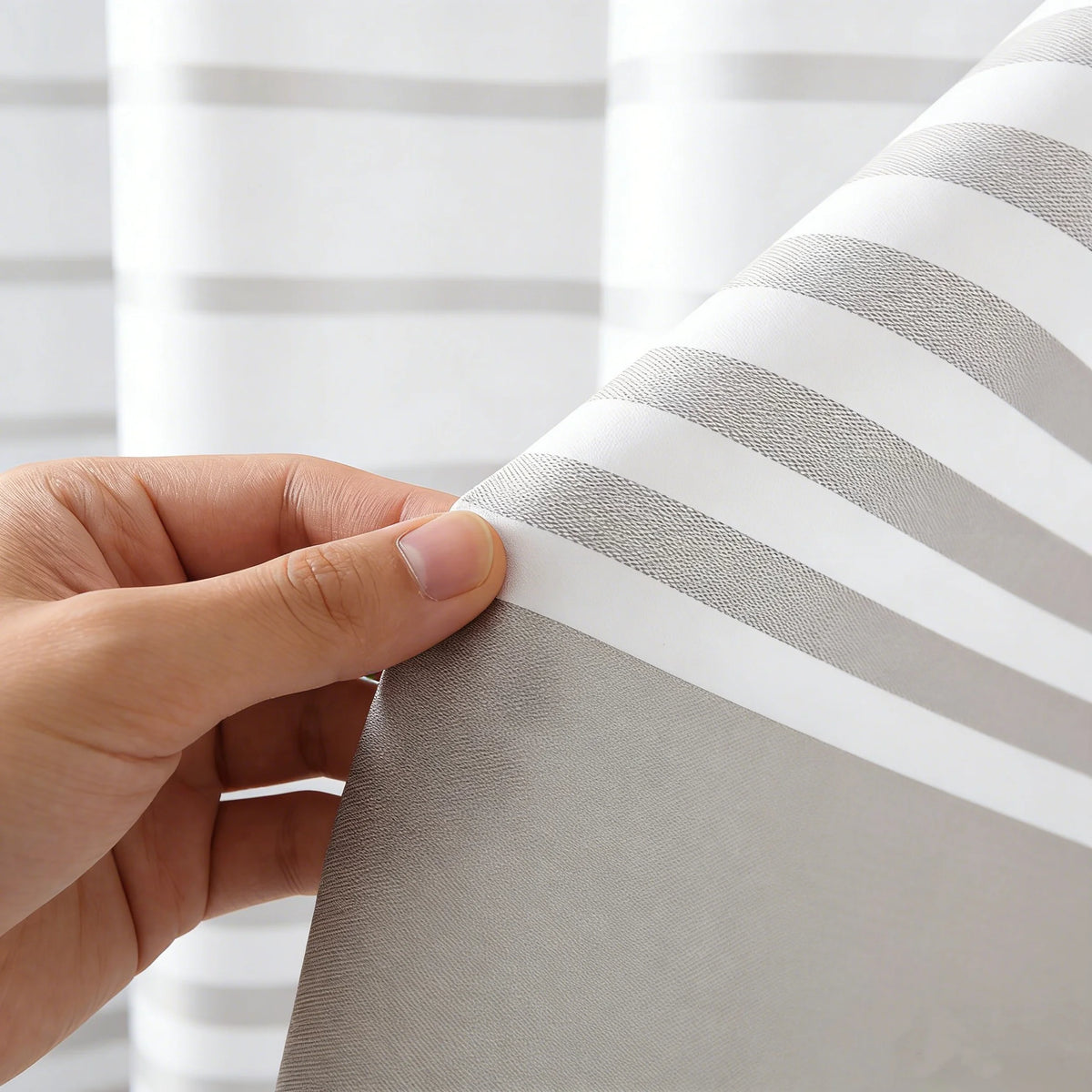 A hand is holding a white and gray striped shower curtain fabric, showing the vertical stripes.
