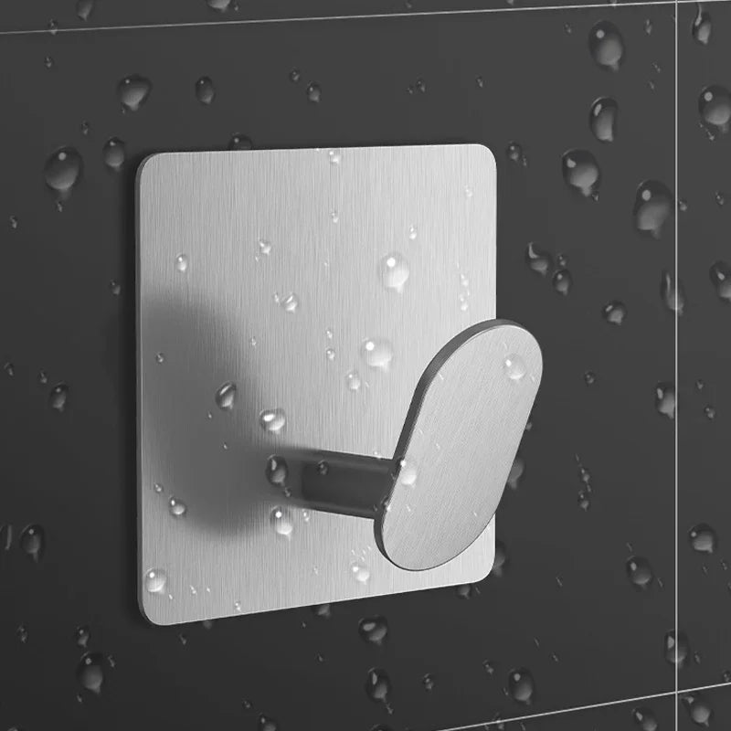 A silver stainless steel adhesive hook mounted on a dark surface with water droplets.