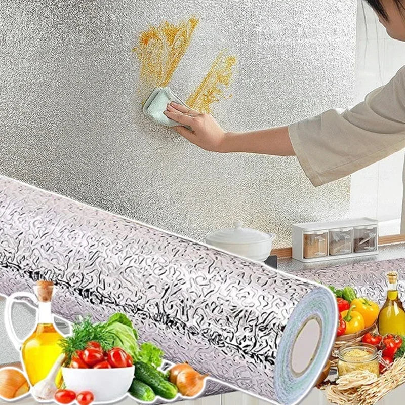 A hand applies a self-adhesive aluminum foil kitchen wall sticker to a textured wall, with the rolled foil and related ingred