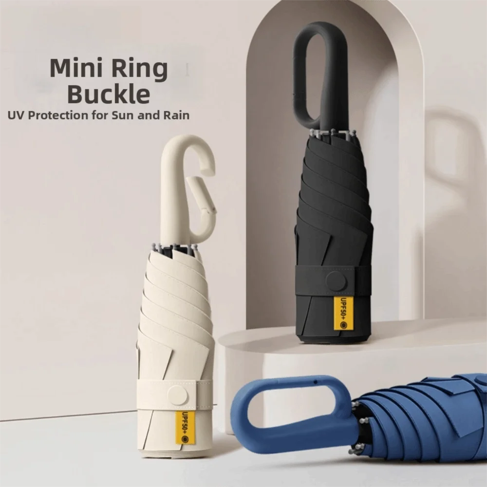 A white mini ring buckle and a black folding umbrella are displayed against a light background.