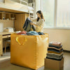 A woman is putting clothes into a yellow heavy-duty waterproof storage bag in a bright room.
