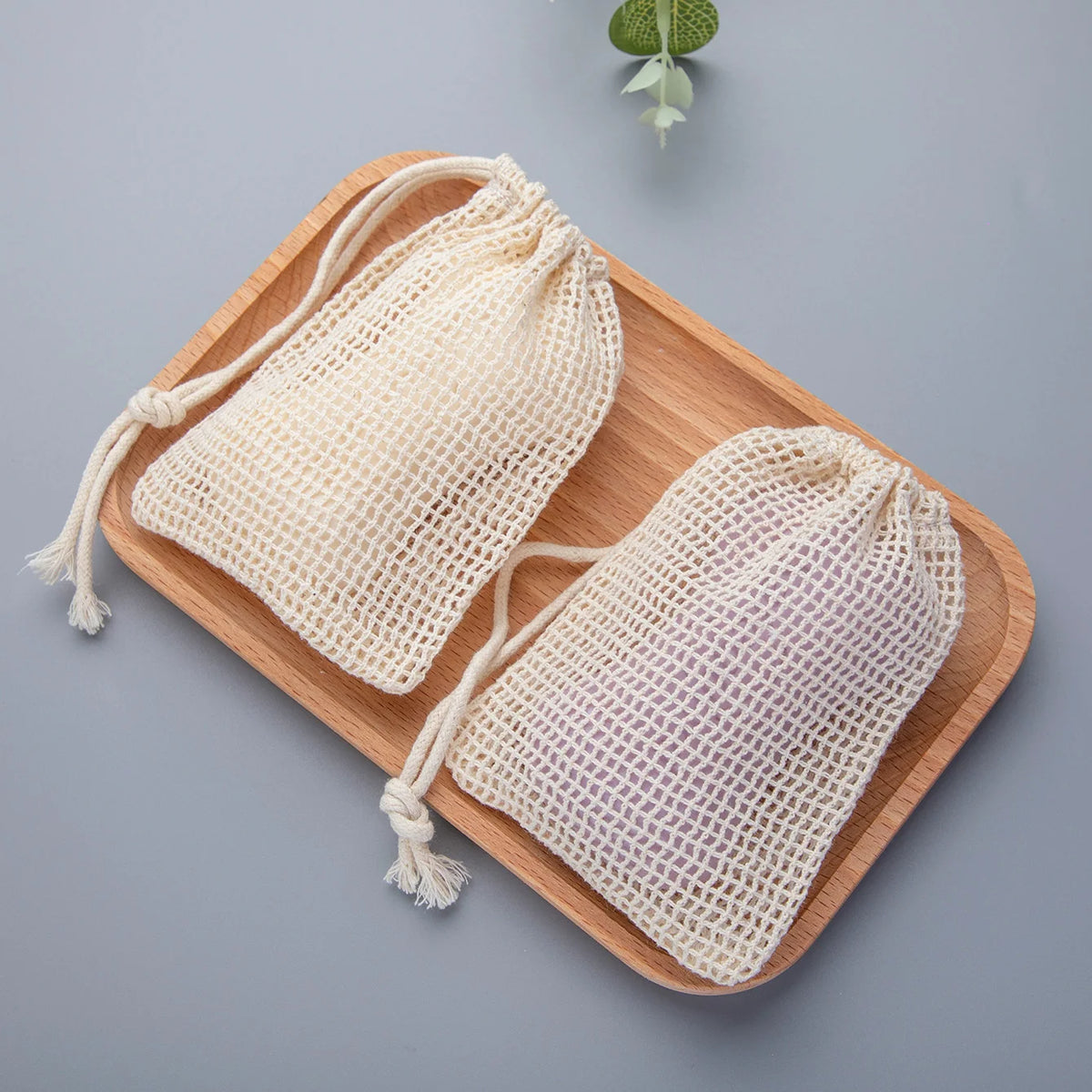 A set of natural cotton mesh soap saver pouches resting on a wooden tray.