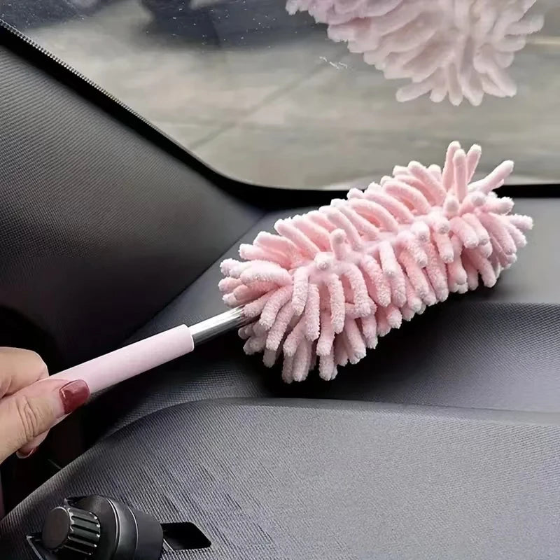 A pink extendable microfiber duster brush is shown being used on a car interior surface.