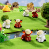 A collection of resin highland cow figurines in white and orange colors arranged on a green grassy landscape.