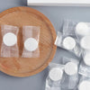 Several sealed packets of white disposable compressed travel towels are arranged on a wooden cutting board.
