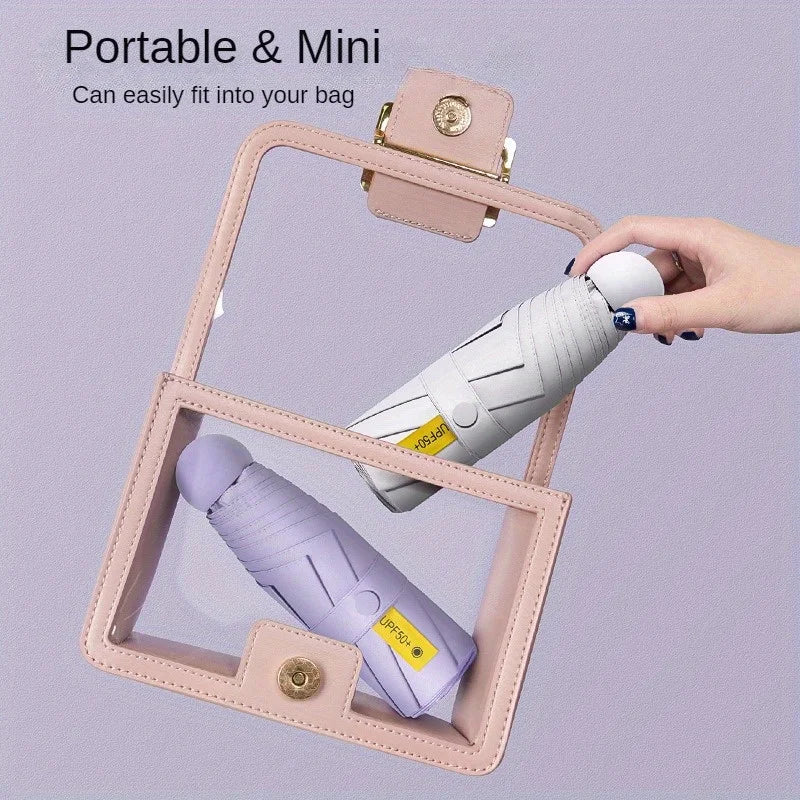 A pink folding umbrella is shown being held by a hand, with another umbrella visible inside a clear plastic frame.