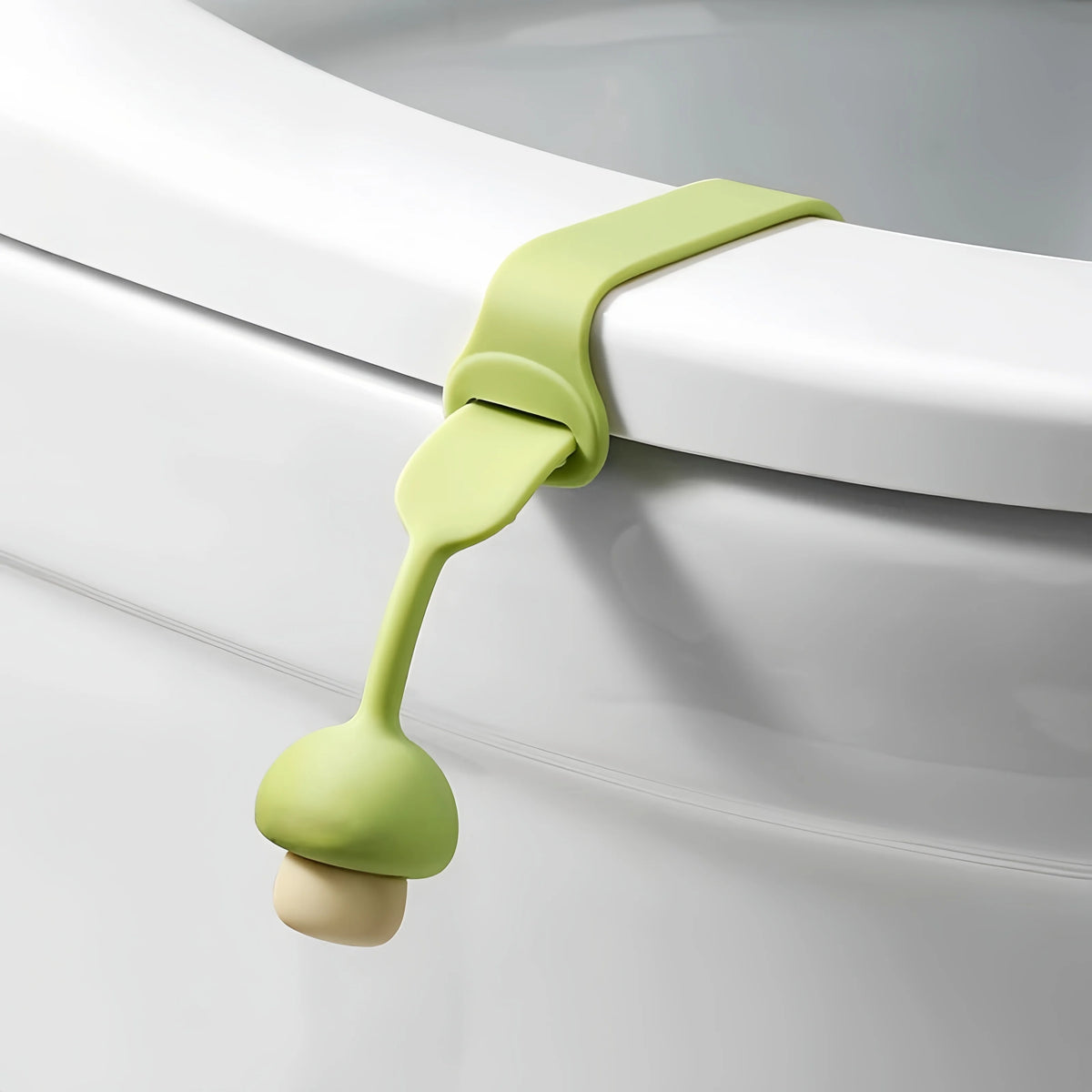 A silicone toilet seat lifter ring opener in light green and beige, shown against a white porcelain surface.