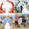 A woman in a white wedding dress stands within an elaborate floral arch decorated with pink, red, and purple flowers.