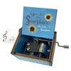 A mini wooden music box with a blue lid featuring the text You Are My Sunshine and a hand crank mechanism.