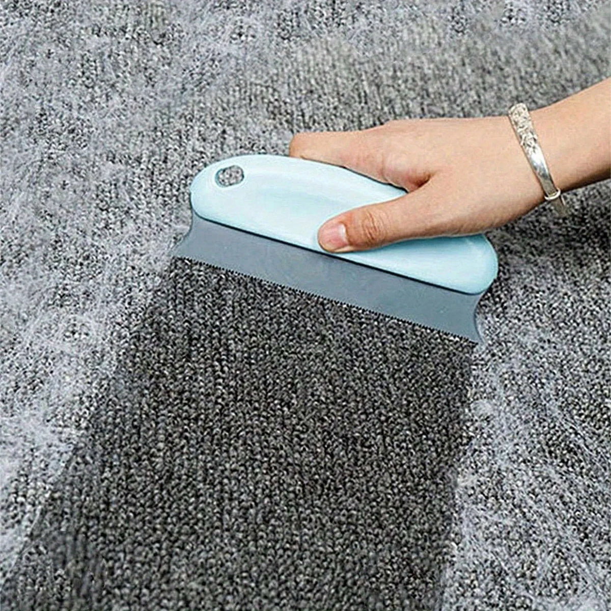 A hand is using a light blue pet hair remover brush on a gray, textured fabric.