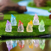 A collection of luminous resin mini fairy gnomes in various pastel colors resting on green grass with a blue stream backgroun