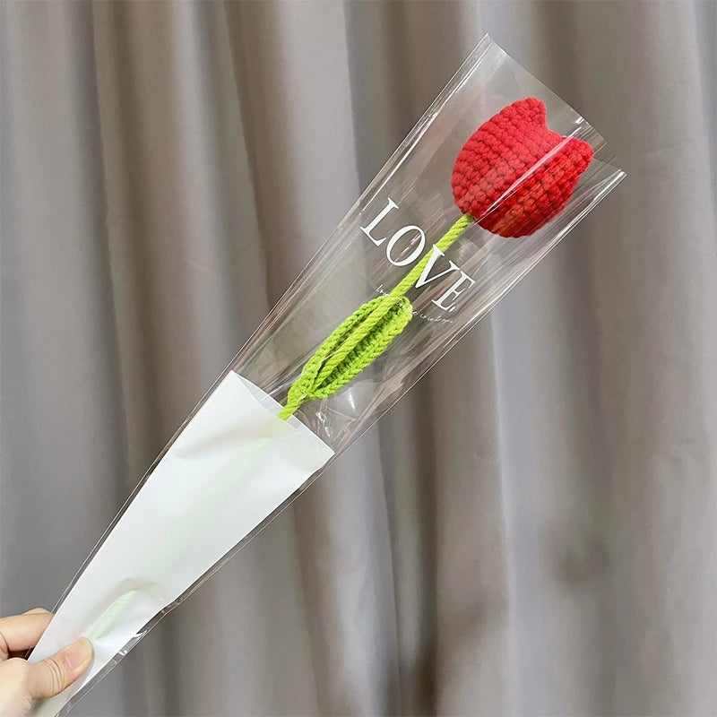 Un bouquet de cœurs en coton fait main avec une fleur rouge et une tige verte, présenté dans une gaine en plastique transpare