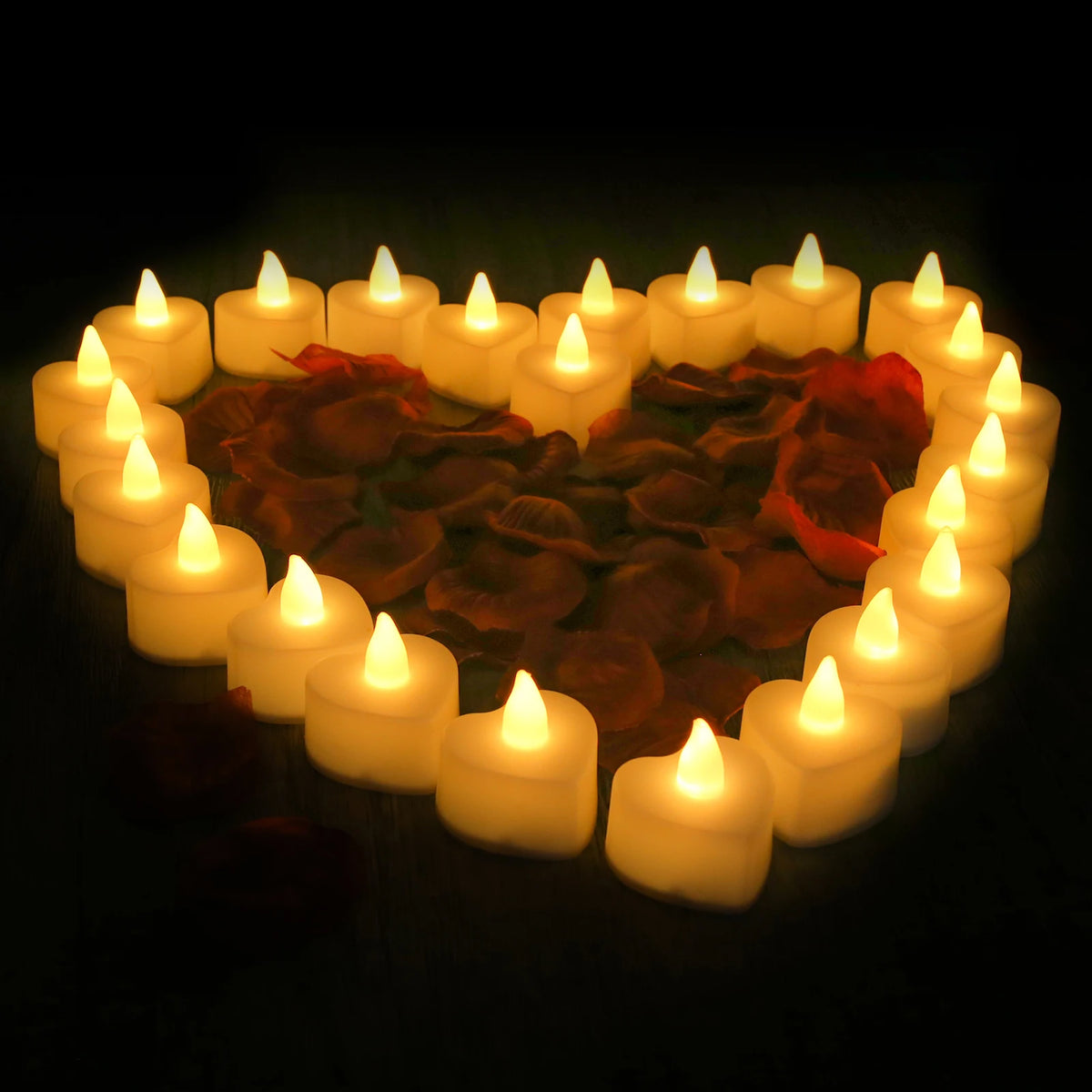 A heart shape formed by glowing LED tea lights surrounded by artificial rose petals.