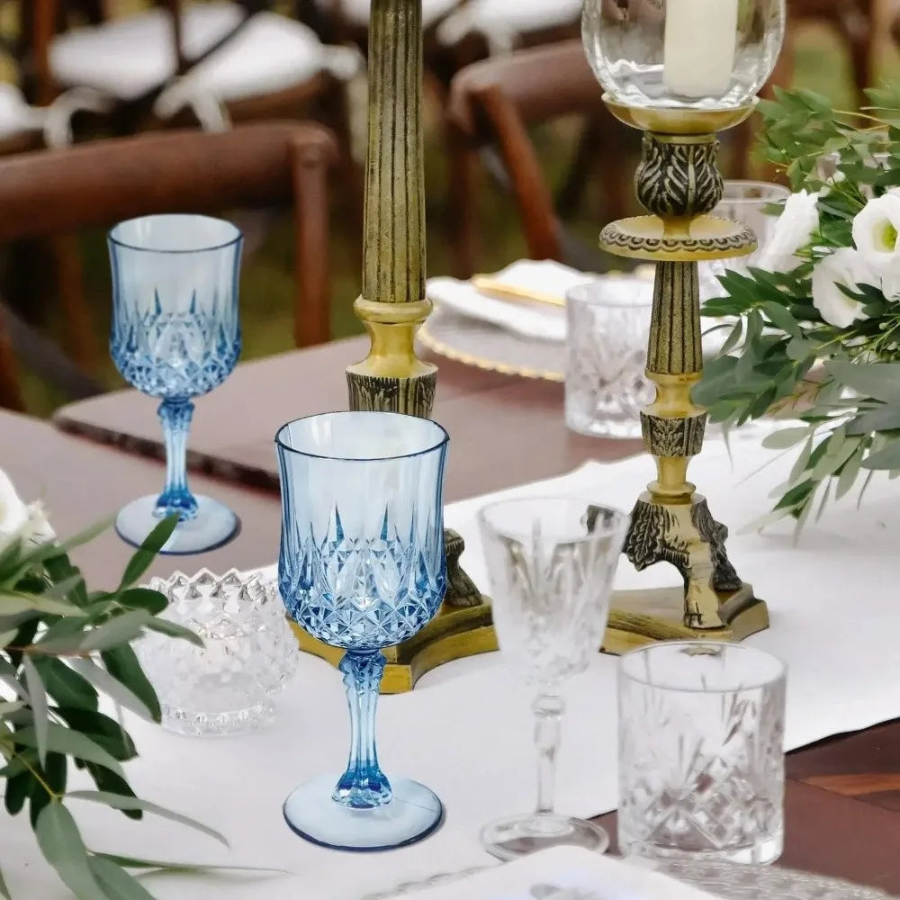 A collection of blue glass champagne flutes and various clear glassware set on a table with greenery.