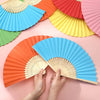 Une main tient un éventail orange pliable à côté de divers éventails en papier et en bambou colorés.