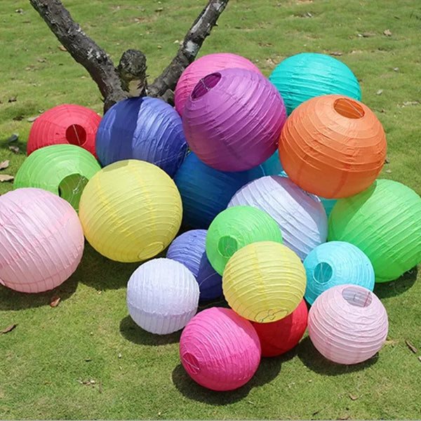 A collection of colorful round paper lanterns in shades of pink, purple, orange, yellow, green, and blue arranged on grass.