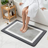 A person sits on a bathtub edge with a gray microfiber bath mat placed on the floor.