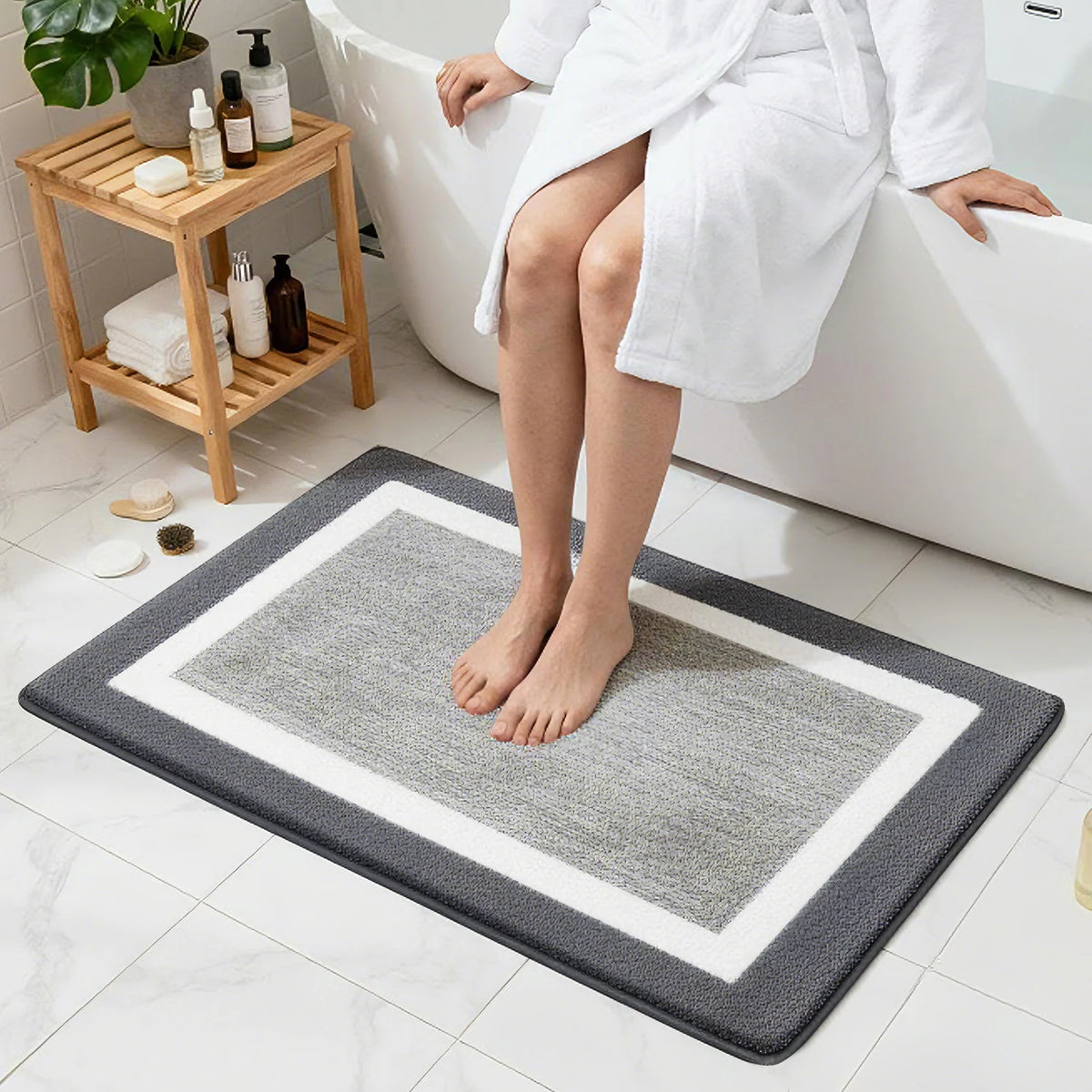 A person sits on a bathtub edge with a gray microfiber bath mat placed on the floor.