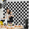 A black and white checkered foil curtain backdrop featuring a baby and cupcakes for a first birthday celebration.