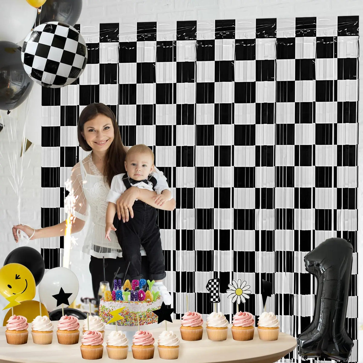 A black and white checkered foil curtain backdrop featuring a baby and cupcakes for a first birthday celebration.