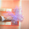 A hand is holding a large, sheer purple and pink simulated butterfly decoration against a light orange background.