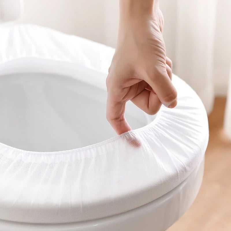 A hand is touching the rim of a white disposable toilet seat to show its texture.