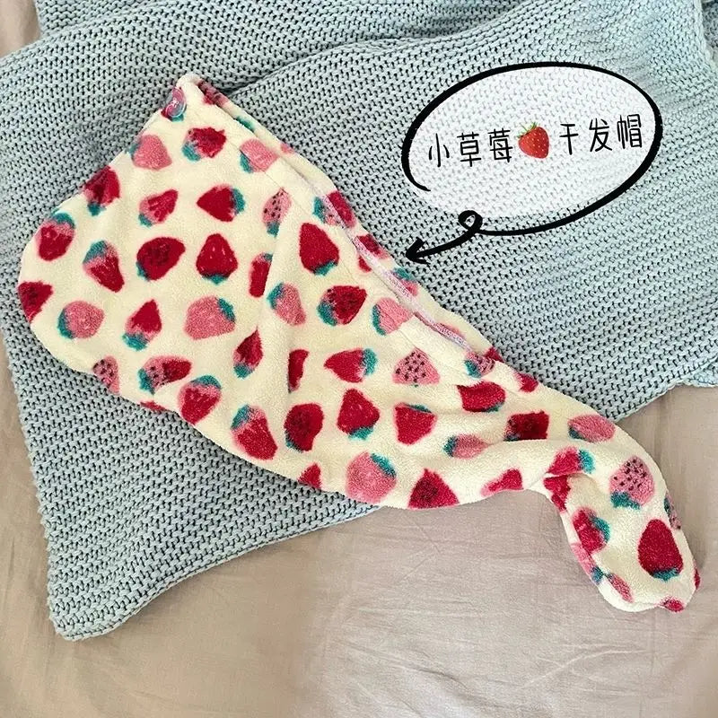 A pink and white strawberry print quick-drying hair towel headscarf is displayed on a light blue knitted fabric.