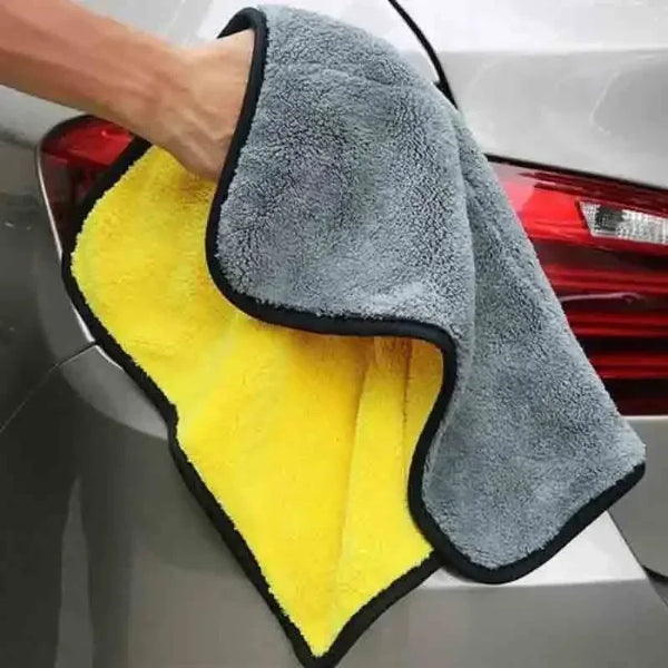 A hand is holding a yellow and gray microfiber cleaning towel, likely for automotive use.