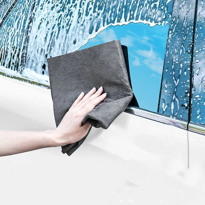 A hand holds a gray microfiber cleaning cloth against a window pane covered in water droplets.