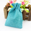 Türkisgrüne gewebte Jute- und Leinen-Geschenktasche mit Schleife, auf einem Holztablett mit rosa Blumen.