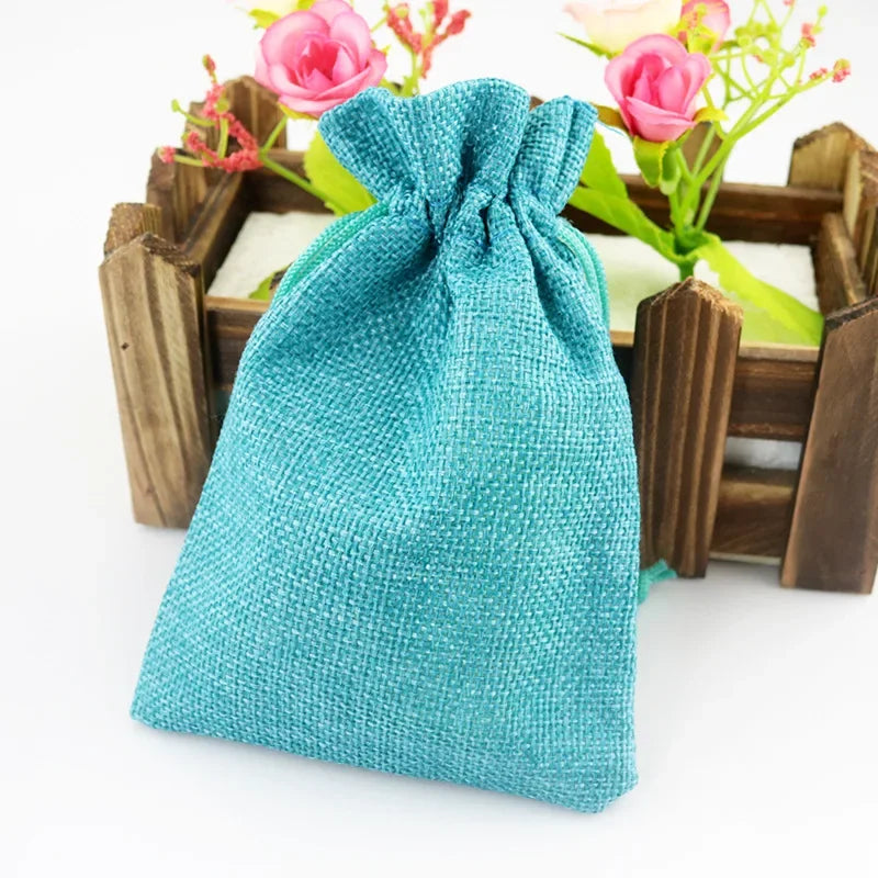 Türkisgrüne gewebte Jute- und Leinen-Geschenktasche mit Schleife, auf einem Holztablett mit rosa Blumen.