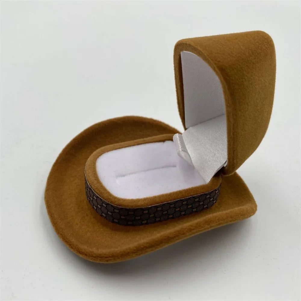 A brown velvet cowboy hat jewelry storage box is shown open, displaying a white insert.