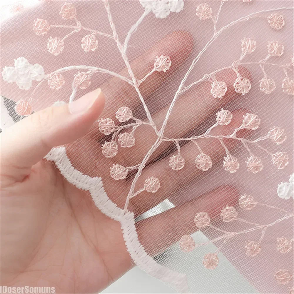 Close-up of sheer pink embroidered fabric with delicate white floral patterns being held by a hand.