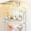 A hand is hanging white and pink knitted items on a white multi-clip drying rack mounted on a wall.