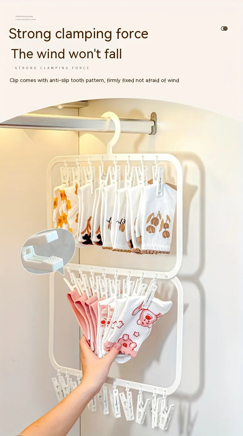 A hand is hanging white and pink knitted items on a white multi-clip drying rack mounted on a wall.