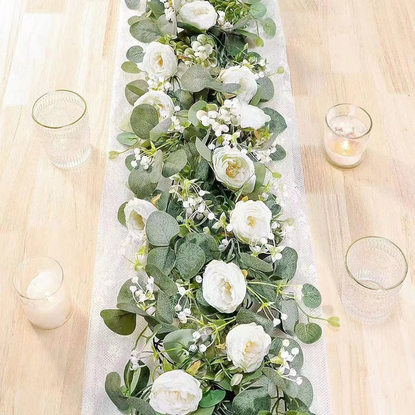 An artificial eucalyptus and rose garland displayed on a white cloth with glass cups.