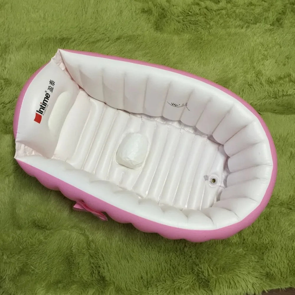 A pink inflatable bath tub for kids is shown lying on a green fuzzy surface.